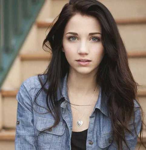 An image of a girl with long brown hair, blue eyes, and a denim jacket.